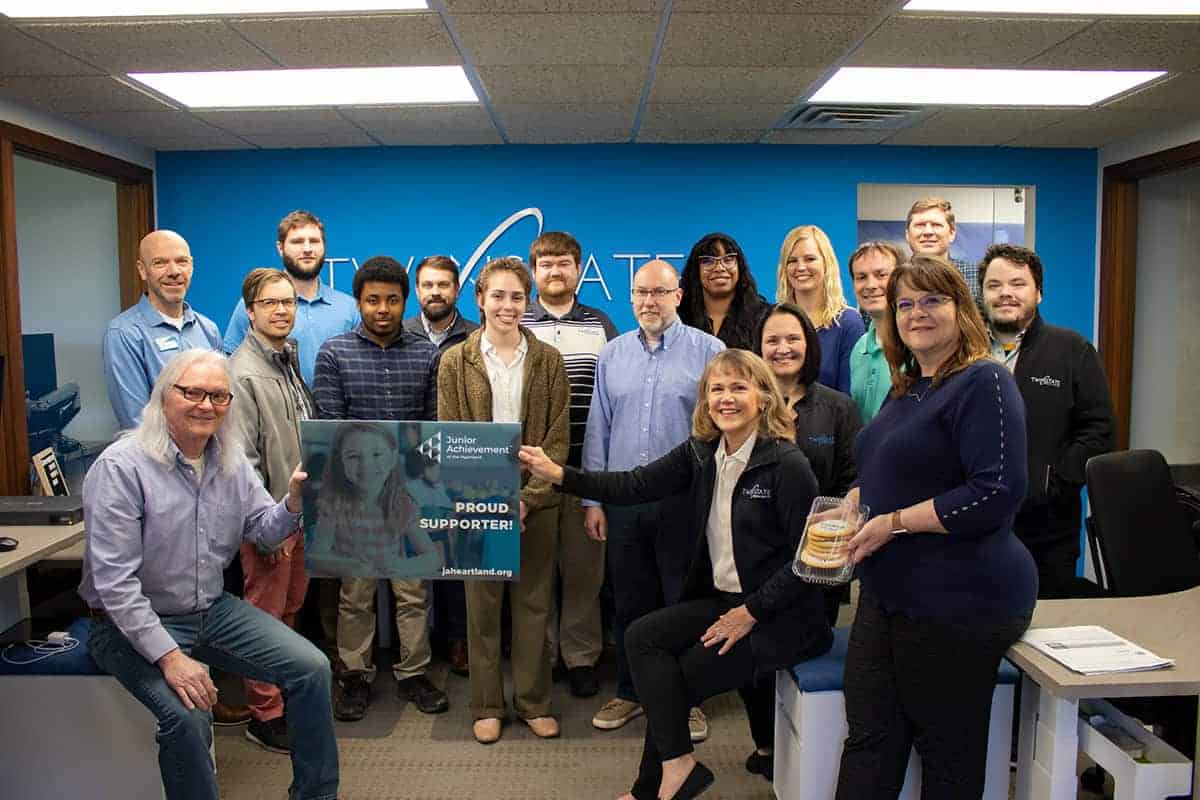 Twin State Technical Services employees gathered around a Junior Achievement Poster.