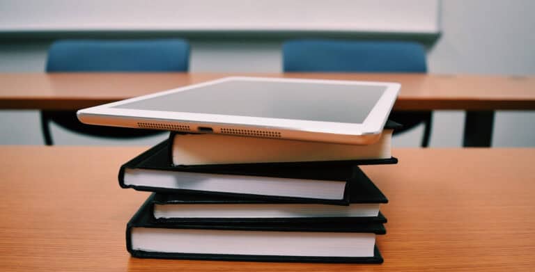 Tablet on top of a stack of notebooks on a classroom desk.