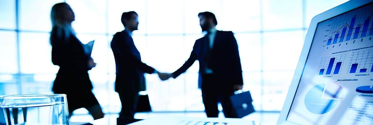 Professional business meeting with handshake, modern office background, technology, and financial data on digital screens - Twin State Technical Services.