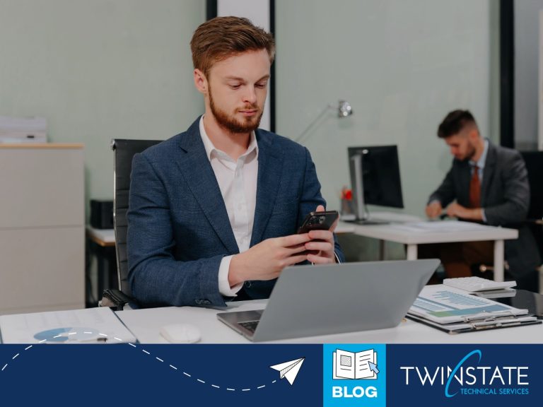 Employee using a smartphone and laptop in an office while practicing workplace cybersecurity habits.