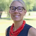 Smiling woman with glasses and red necklace outdoors in a park setting, representing professional and friendly service in the Quad Cities area.